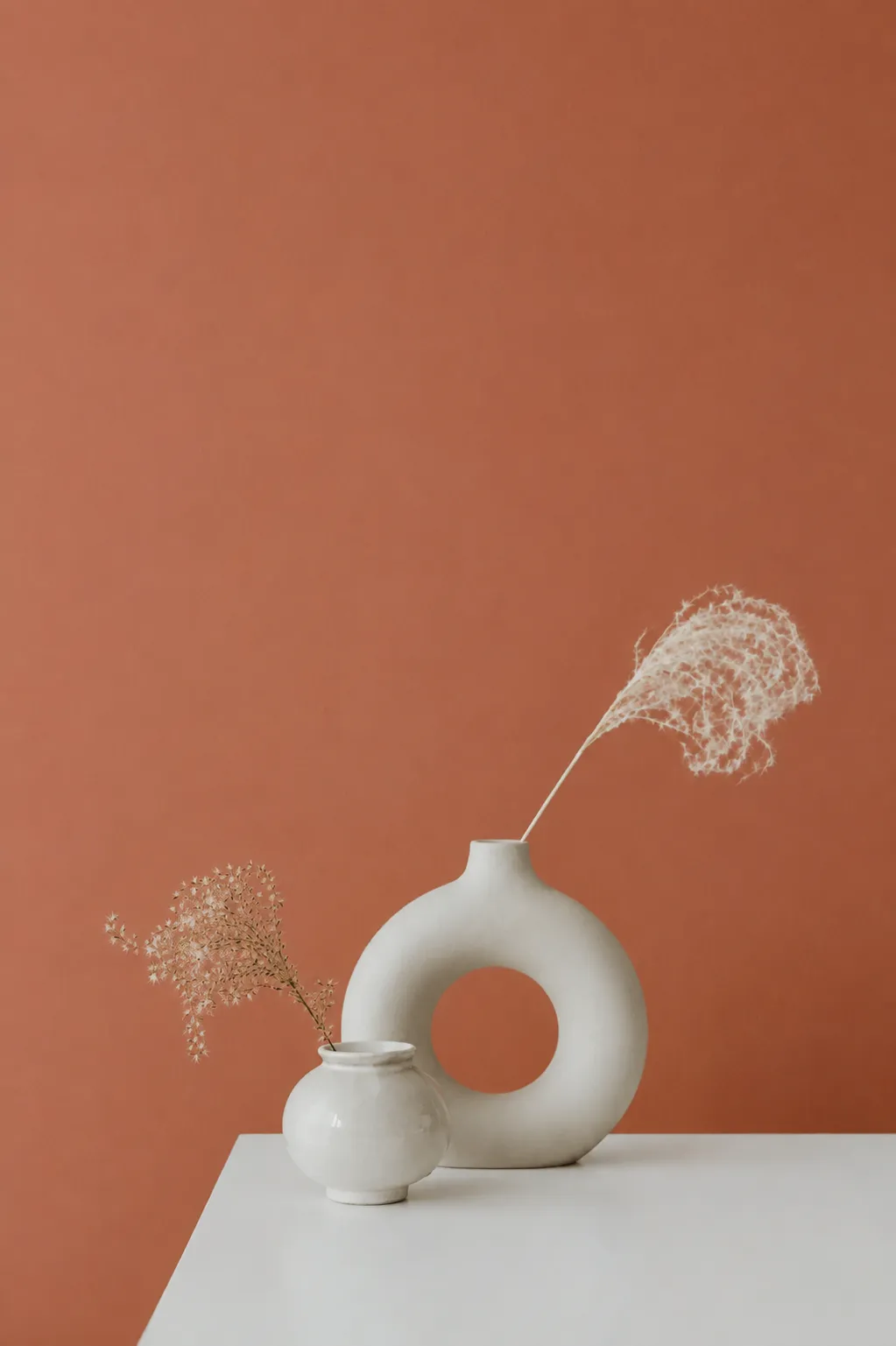 Vases en céramique blanche et herbes séchées devant un mur terracotta